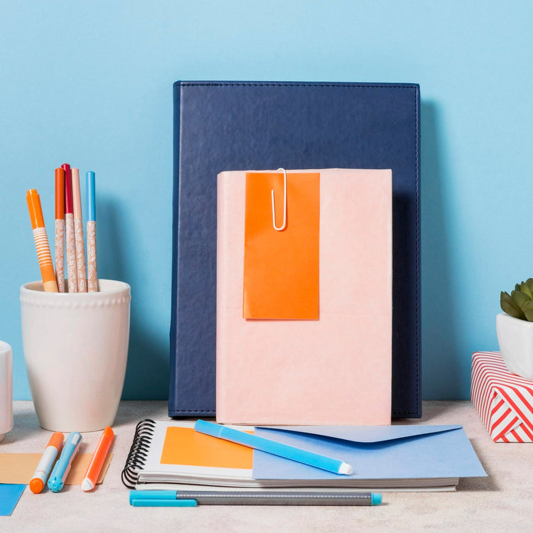Notebooks, pens, and a mug on a desk with a blue background