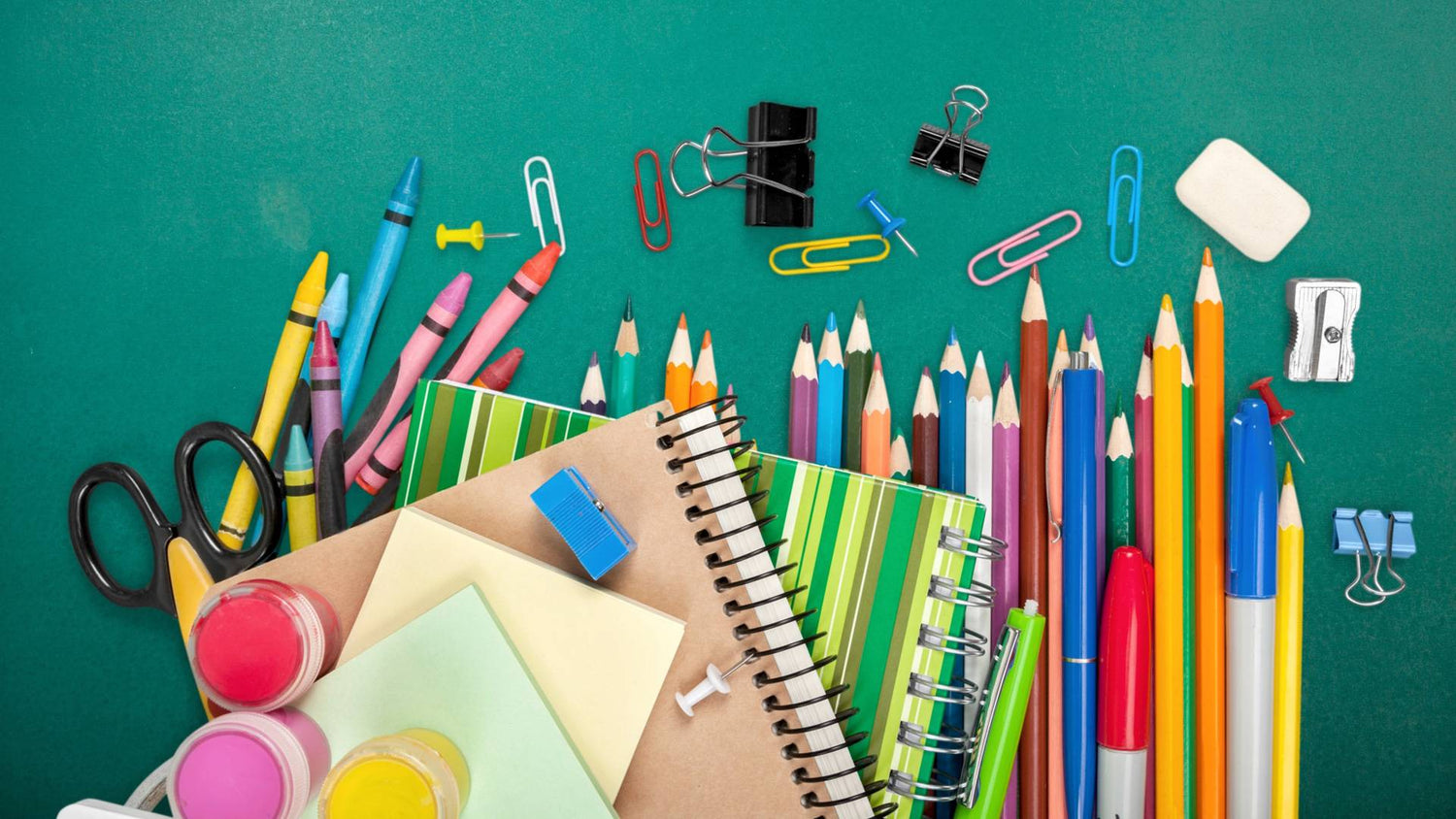 Assorted school supplies including pencils, crayons, and notebooks on a green background